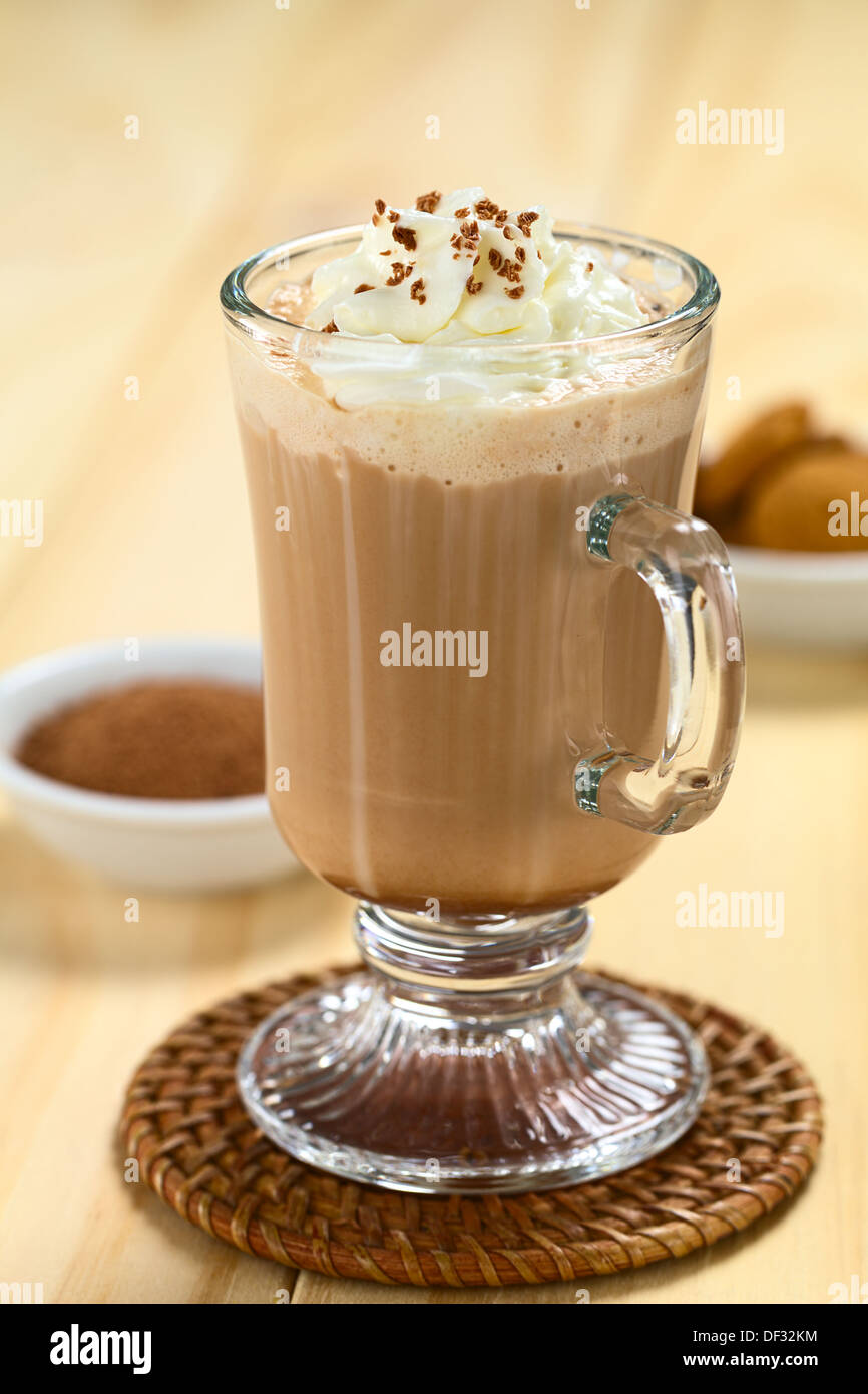 Cioccolata calda con panna montata e scaglie di cioccolato sulla parte superiore, con la polvere di cacao e i cookie nel retro Foto Stock