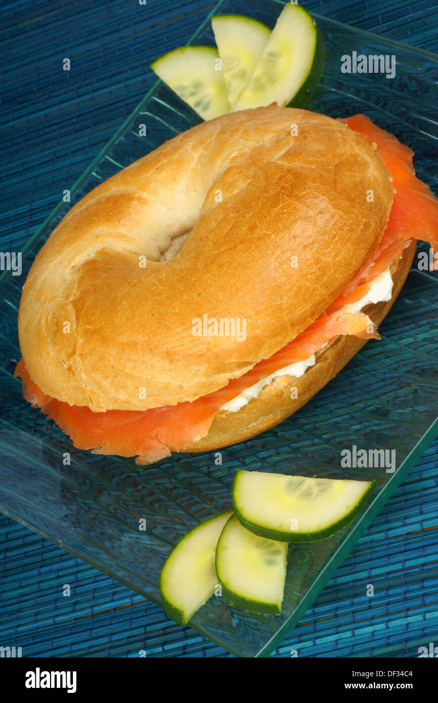 Bagel con formaggio morbido e salmone affumicato con fette di cetriolo servita su un vetro trasparente piatto. Foto Stock