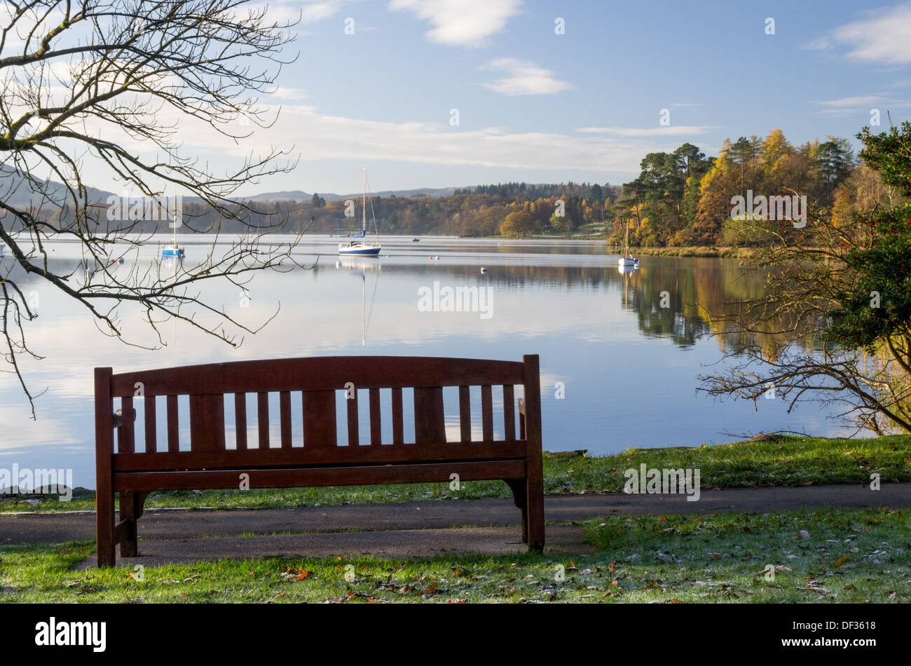 Una vista da un banco in un lago-side park vicino a Ambleside in una mattina di sole con dello specchio d'acqua e barche in distanza. Foto Stock
