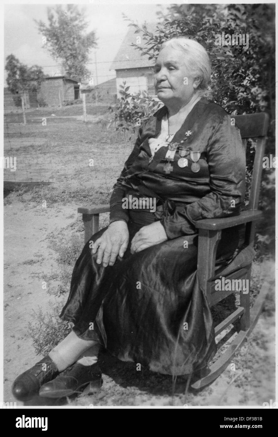Un'anziana donna nativa americana viene vista seduta su una sedia a dondolo, catturata in una fotografia storica come parte della collezione U.S. National Archives, che riflette la vita e la cultura. Foto Stock