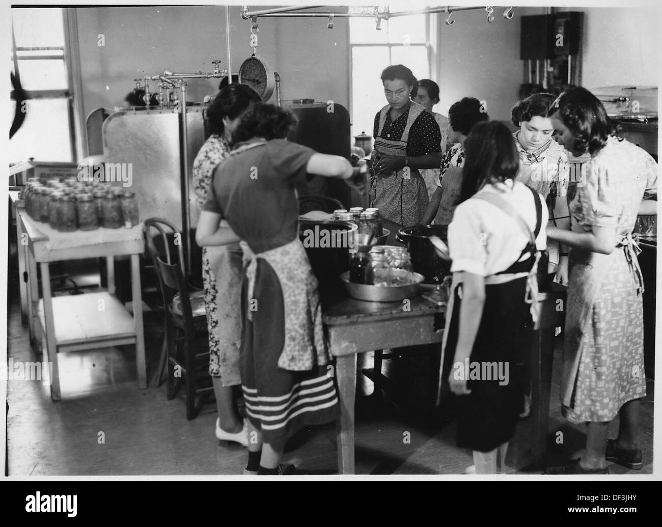 Questa immagine raffigura l'inscatolamento dei prodotti, probabilmente come parte di un processo agricolo più ampio. Il Canning era un metodo comune per preservare il cibo per lo stoccaggio e la distribuzione a lungo termine, specialmente nelle comunità rurali o agricole. Foto Stock