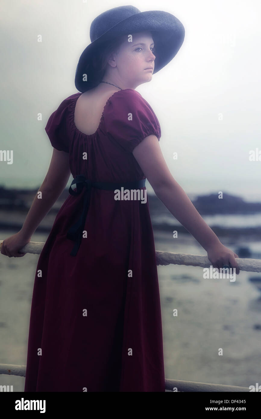 Una giovane ragazza in un abito rosso è in piedi a una ringhiera in bianco al mare Foto Stock