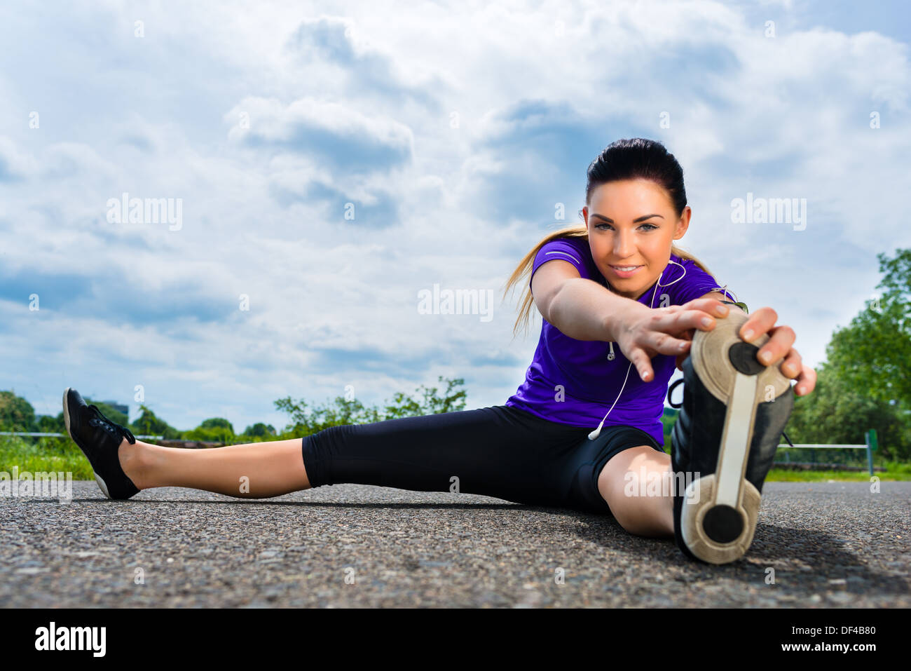 Urban sport - giovane donna sta facendo il riscaldamento prima di eseguire in greenfield su un giorno di estate Foto Stock