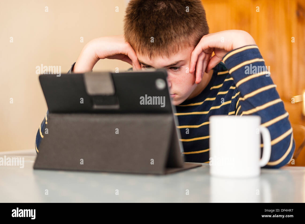 Un ragazzo di 13 anni guardando al suo computer tablet in cucina Foto Stock