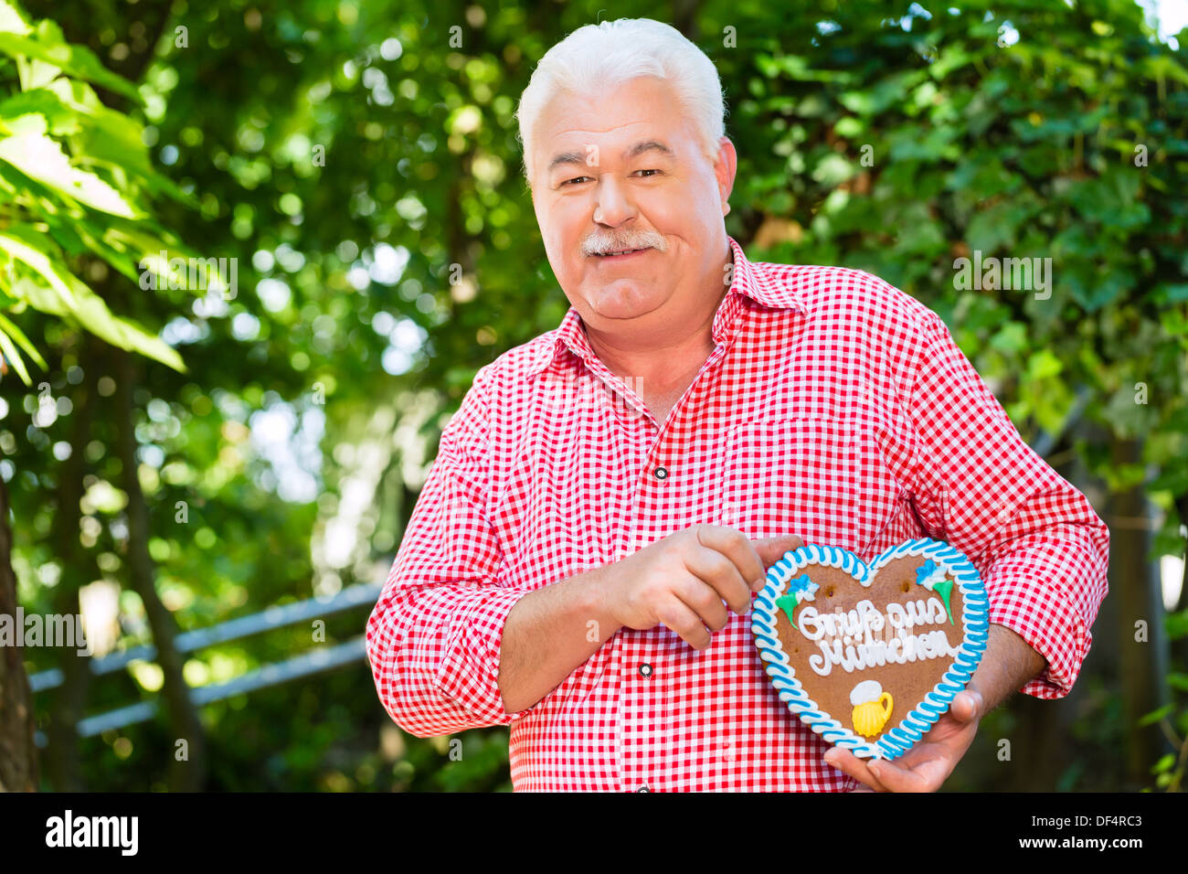 Senior in tradizionali bavaresi vestiti o tracht con lederhosen e panpepato cuore di souvenir in beergarden su Oktoberfest Foto Stock