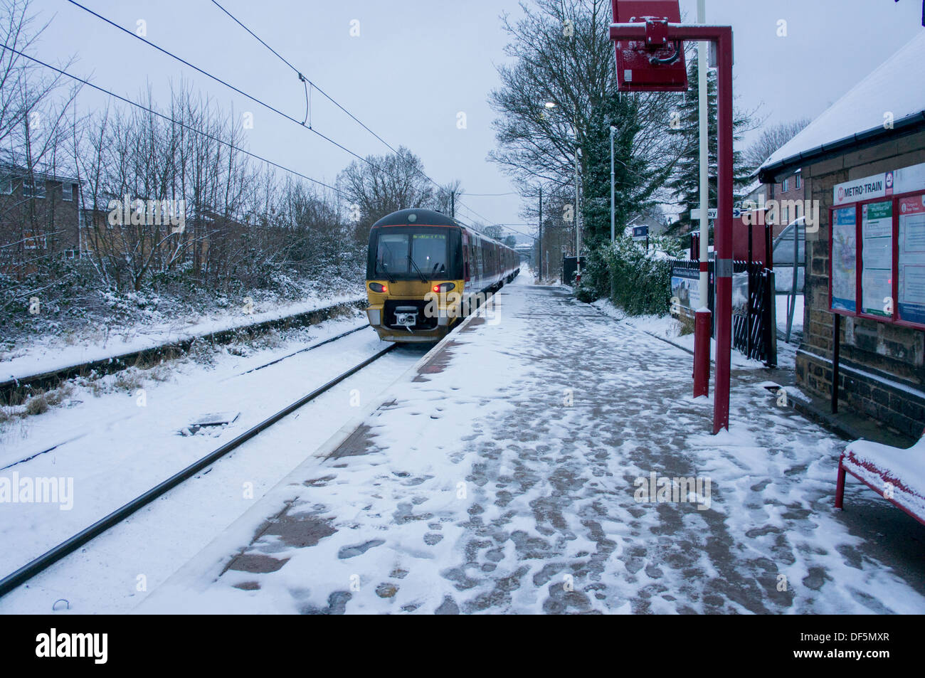 Treno in arrivo & tirando in deserta stazione ferroviaria dopo la nevicata, impronte sulla piattaforma & neve sulle vie - baildon, shipley, Inghilterra, Regno Unito. Foto Stock
