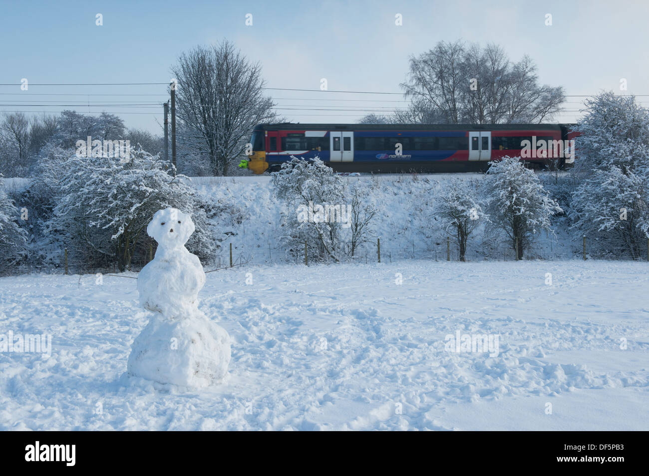Viaggio in treno nelle fredde giornate invernali, lungo la linea ferroviaria il passante singolo pupazzo di neve in piedi in coperta di neve sul campo - Burley in Wharfedale, Inghilterra, Regno Unito. Foto Stock