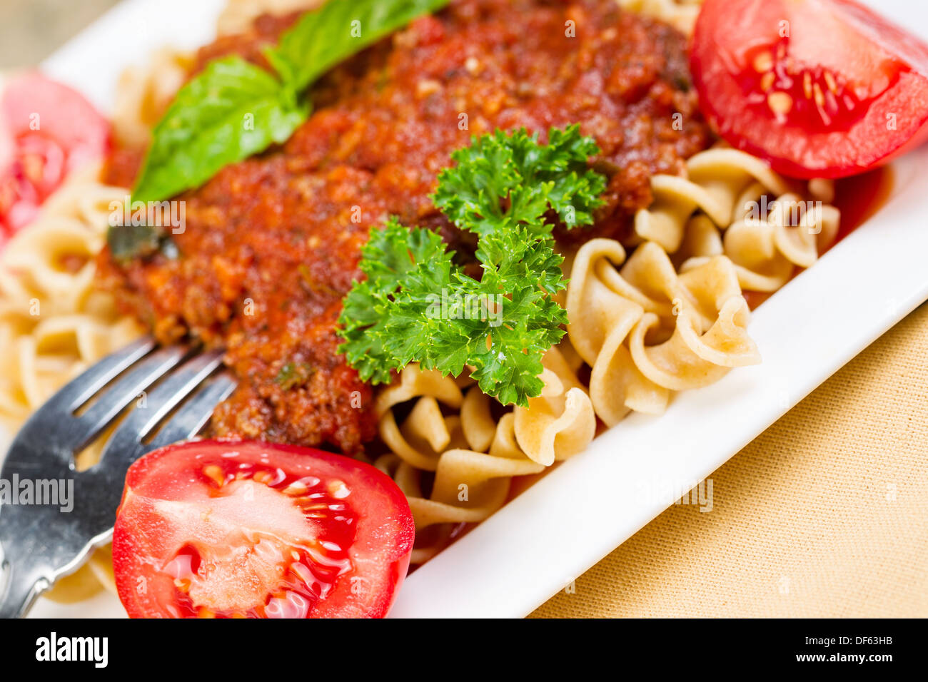 Closeup foto orizzontale di pasta fresca, forcella, salsa di pomodoro, i pomodori, il prezzemolo, il basilico in una piastra bianca Foto Stock