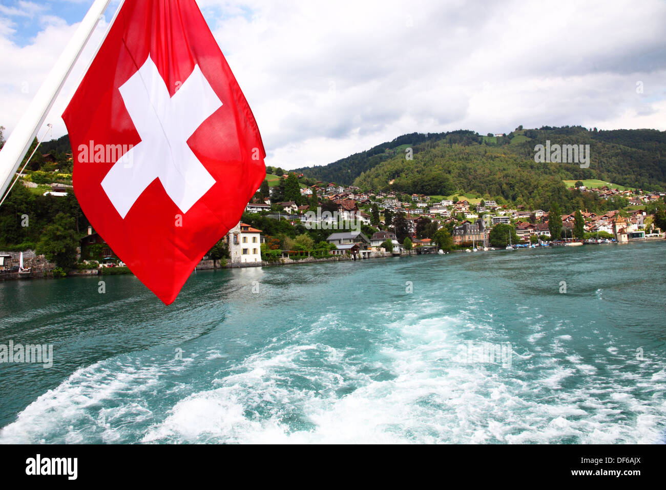 Una bandiera svizzera vola da poppa di un sistema per la cottura a vapore sul lago come si lascia la città di Oberhofen sul Lago di Thun. Foto Stock