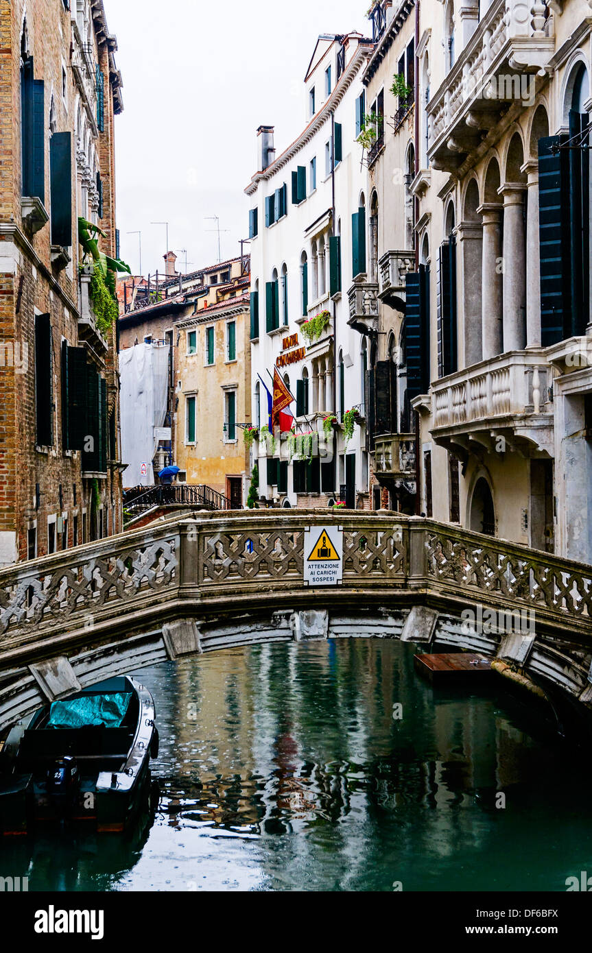 Un turista portando un ombrello per tenere la pioggia off attraversa un piccolo ponte sopra un canale delimitato da edifici alti, Venezia Foto Stock