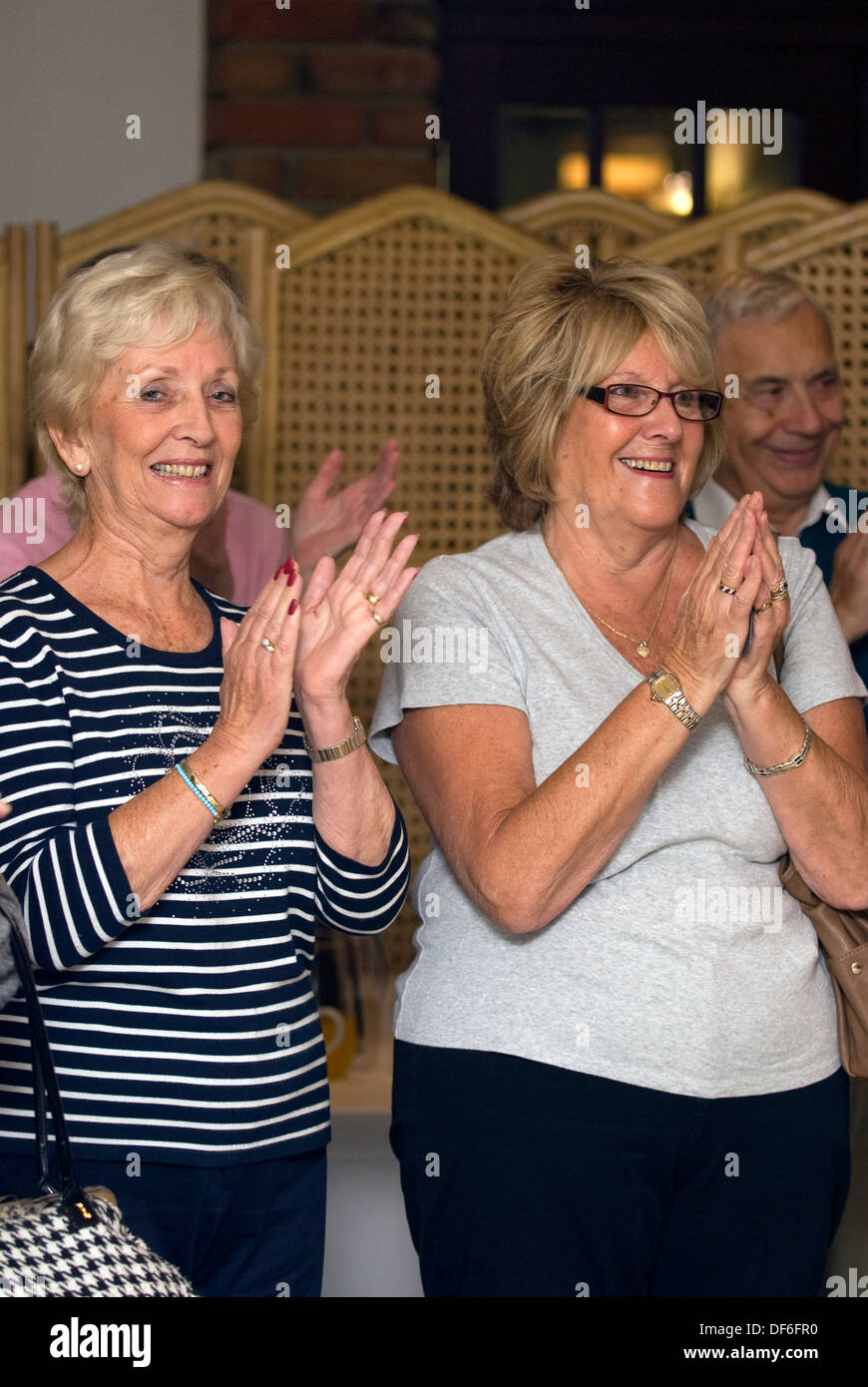 Le donne anziane che mostrano il loro apprezzamento per l'intrattenimento (coro) a macmillan cancer support mattina caffè, surrey, Regno Unito Foto Stock