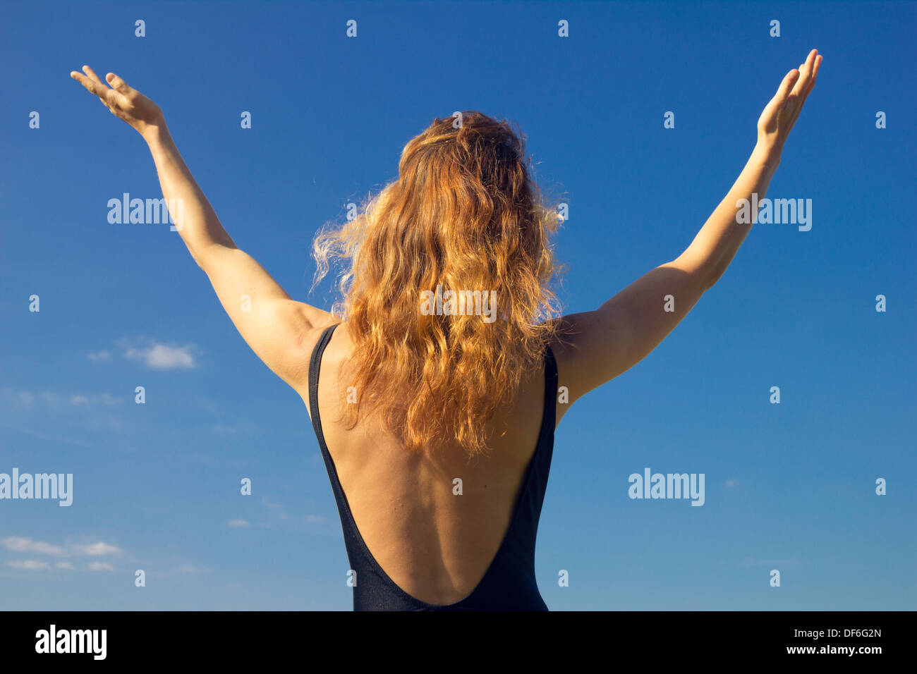 Giovane donna che si allunga le braccia contro il cielo in una giornata di sole Foto Stock