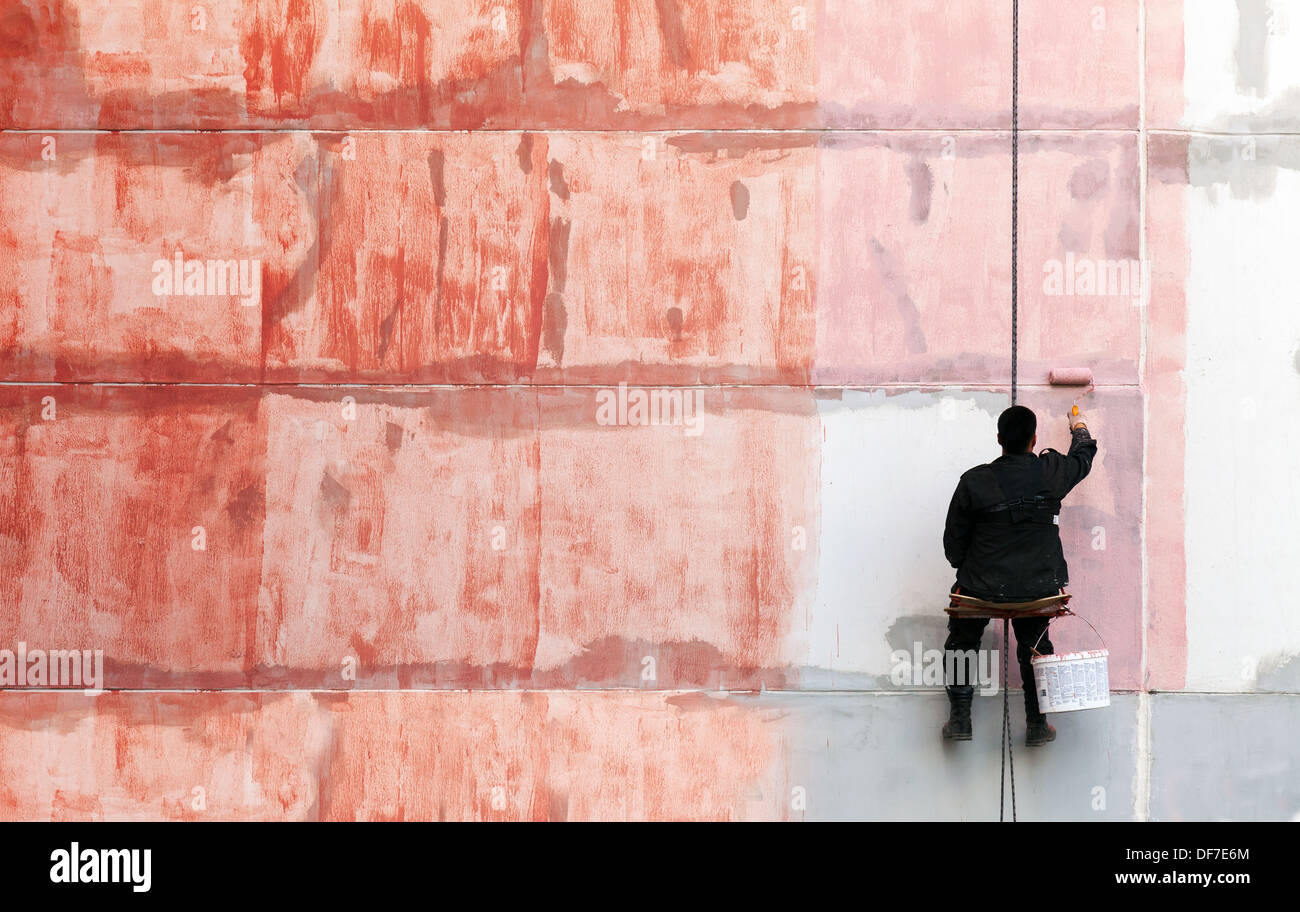 Pittore lavora sul lato esterno della parete edilizia rosso con vernice di adescamento Foto Stock
