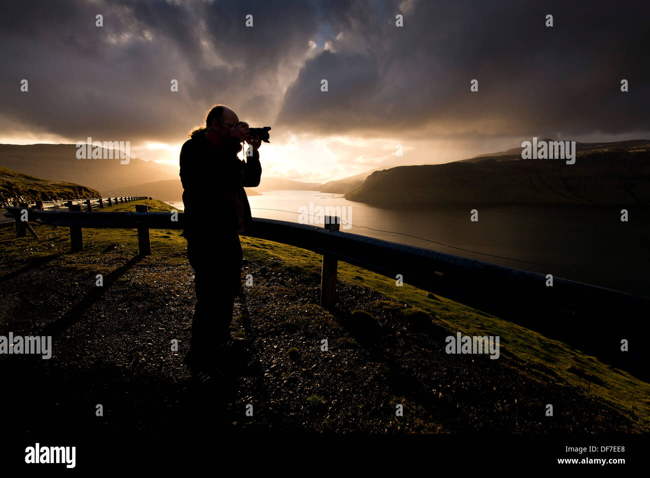 Silhouette di un fotografo in piedi nella parte anteriore del drammatico, nubi atmosferiche, Streymoy, Isole Faerøer, Danimarca Foto Stock