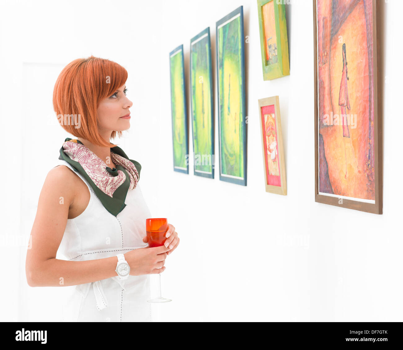 Giovani caucasici redhead donna in piedi in un museo ammirando colorati dipinti incorniciati Foto Stock