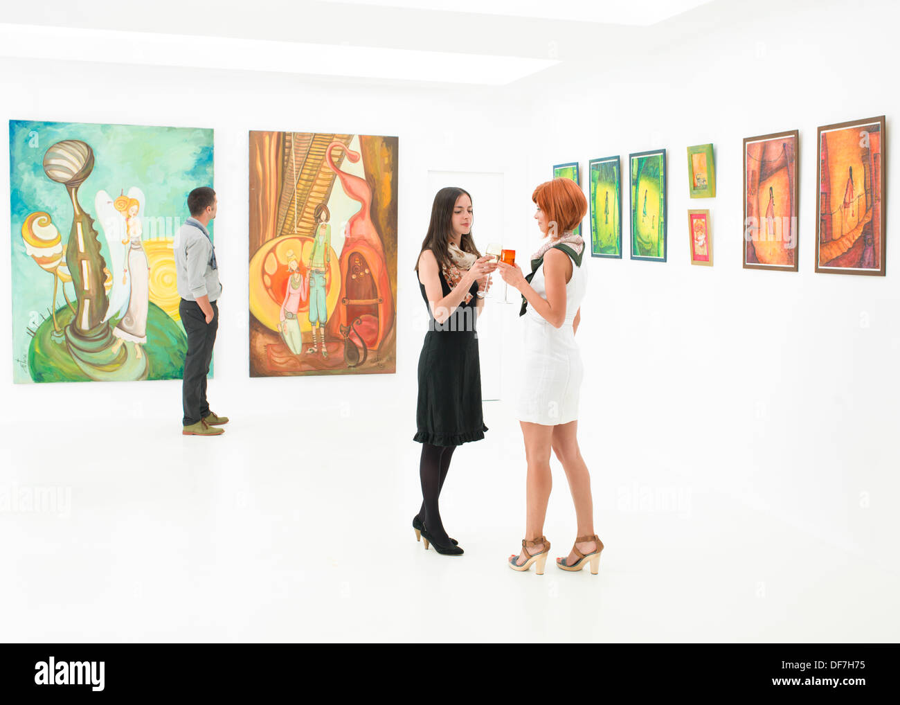 Due donne in piedi e bersi un drink in una galleria d'arte Foto Stock