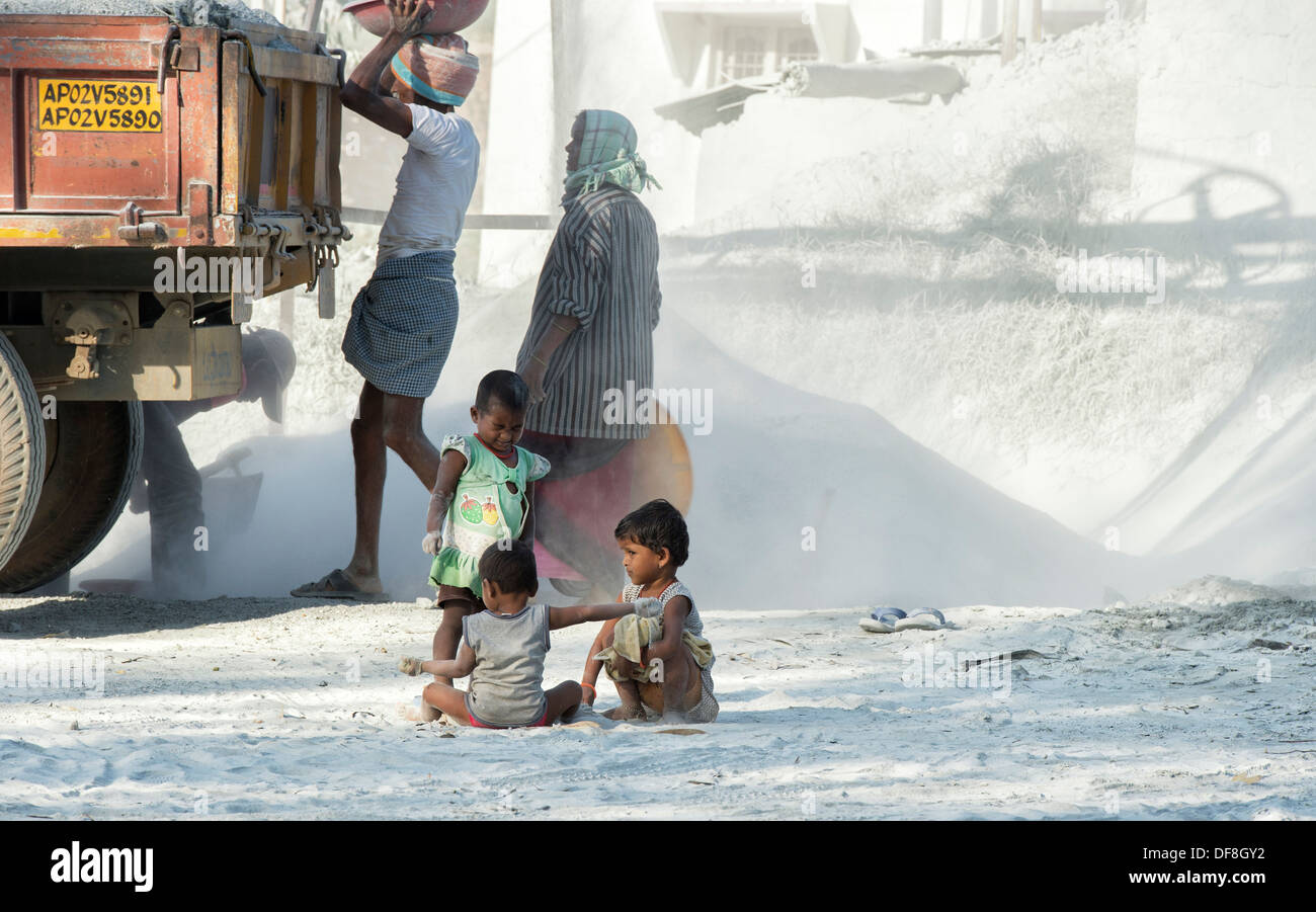 Indian i bambini giocando, circondato da polvere e non protetta, a una frantumazione della pietra opere. Andhra Pradesh, India Foto Stock