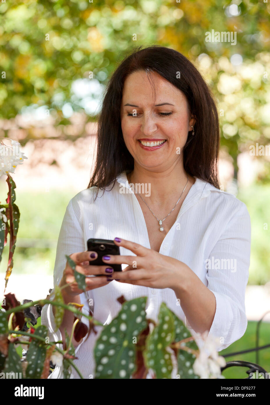 Di mezza età donna caucasica utilizzando smart phone in giardino Foto Stock