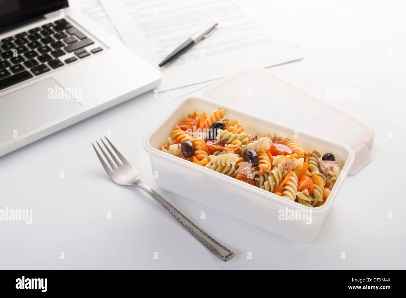 Mangiare un insalata di pasta con verdure e tonno in ufficio Foto Stock