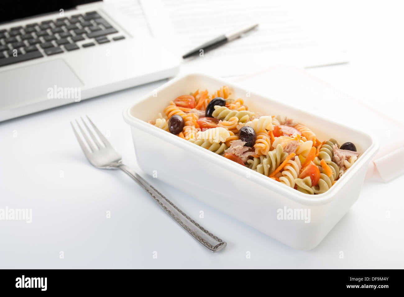 Mangiare un insalata di pasta con verdure e tonno in ufficio Foto Stock