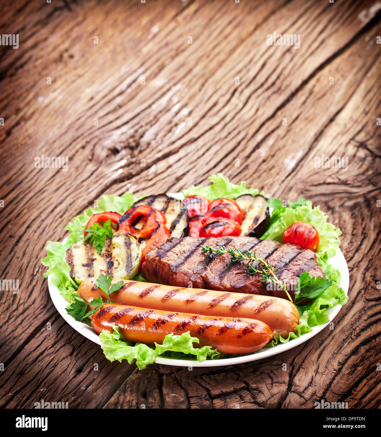 Bistecca alla griglia,salsicce e verdure sopra le foglie di lattuga su un tavolo di legno. Foto Stock