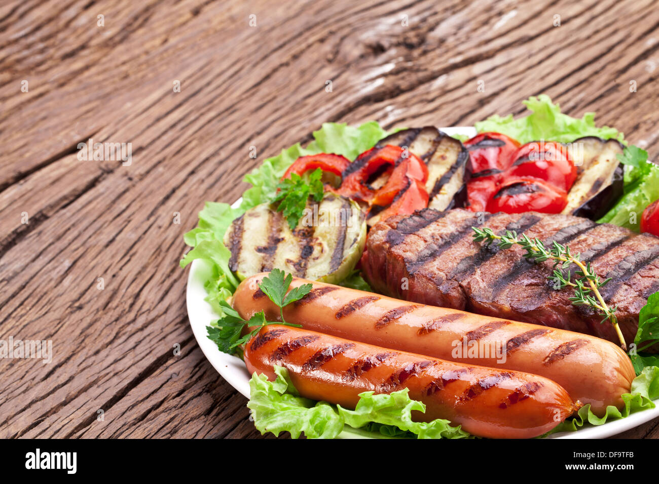 Bistecca alla griglia,salsicce e verdure sopra le foglie di lattuga su un tavolo di legno. Foto Stock