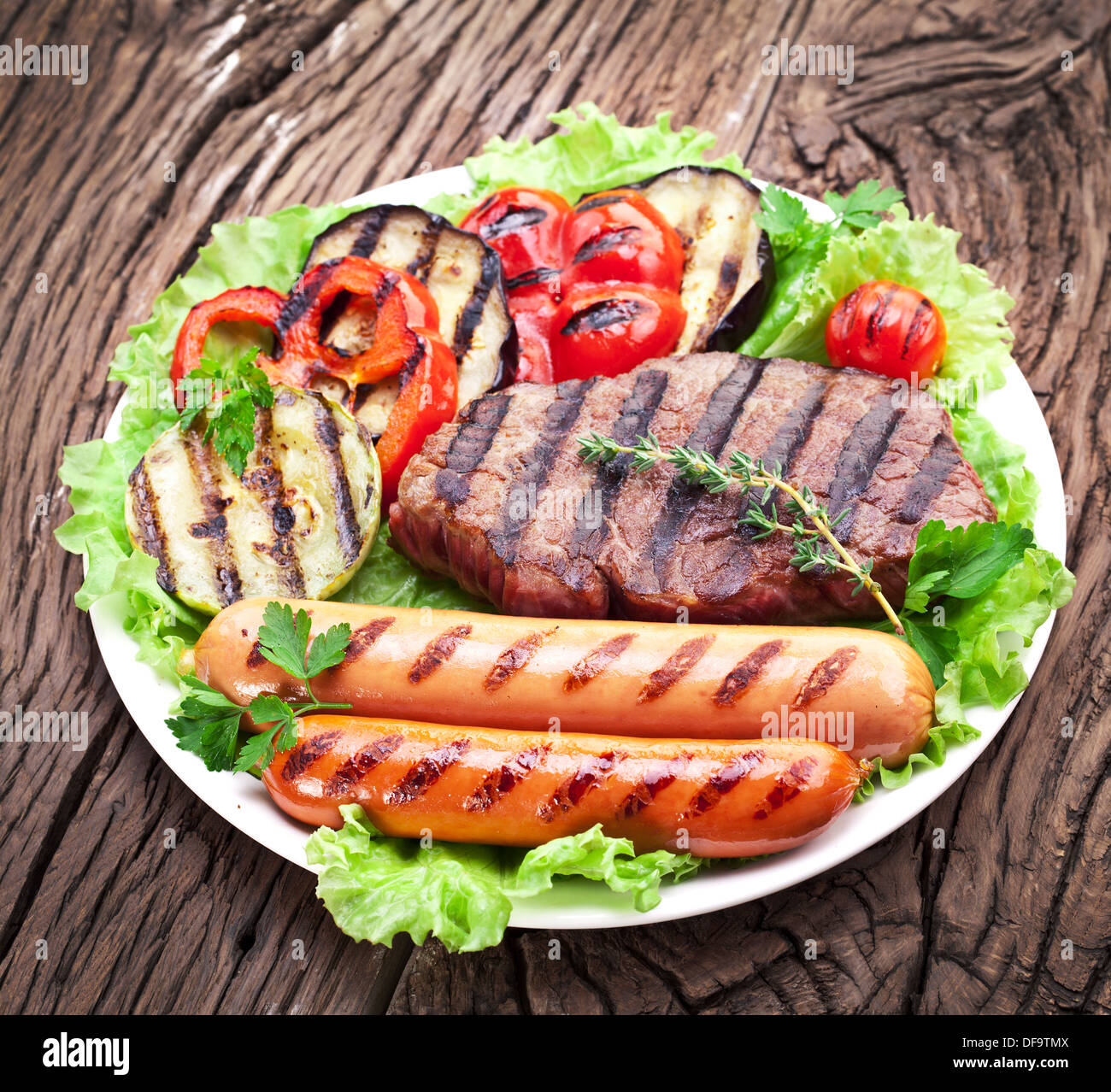 Bistecca alla griglia,salsicce e verdure sopra le foglie di lattuga su un tavolo di legno. Foto Stock