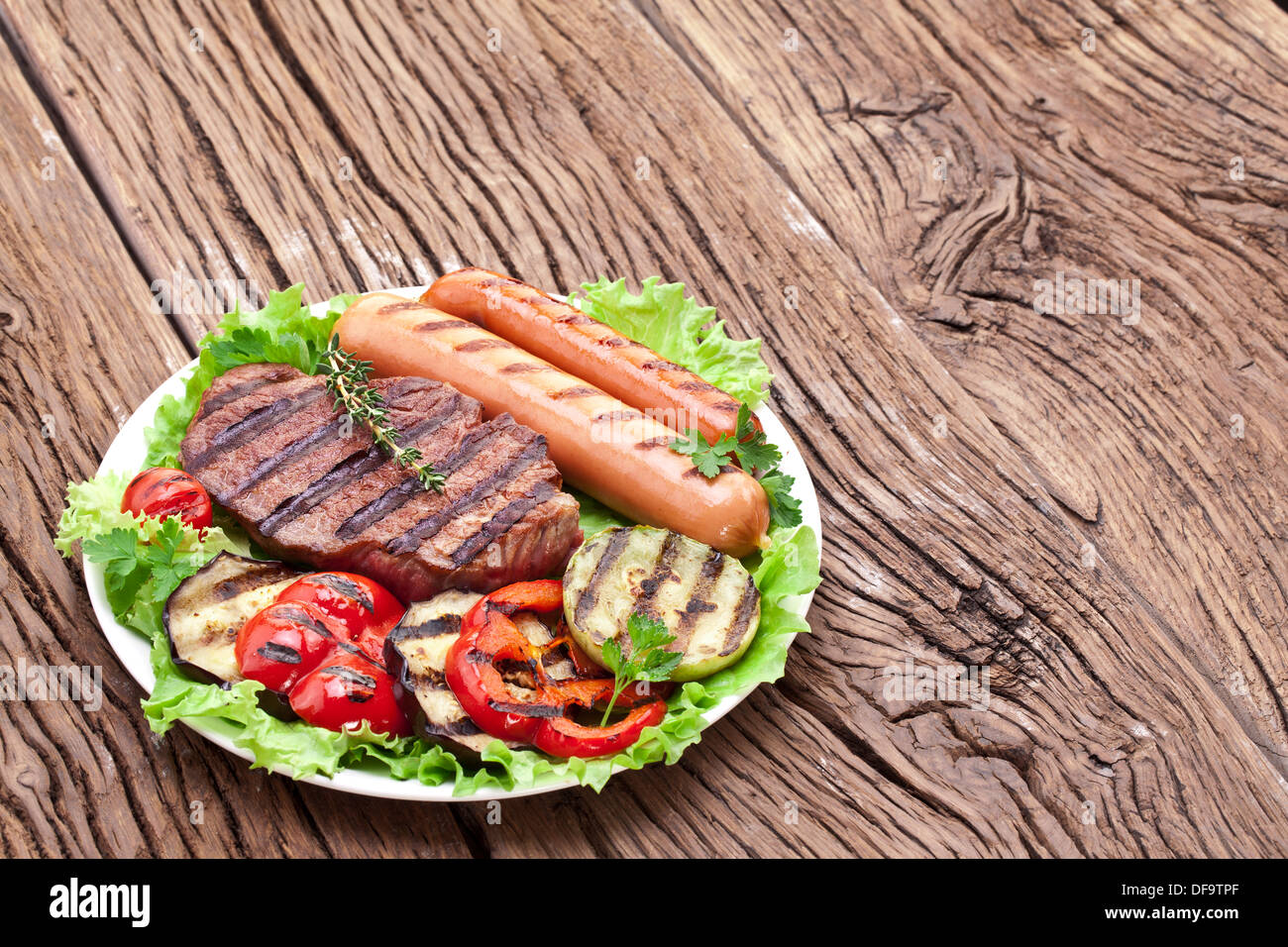 Bistecca alla griglia,salsicce e verdure sopra le foglie di lattuga su un tavolo di legno. Foto Stock