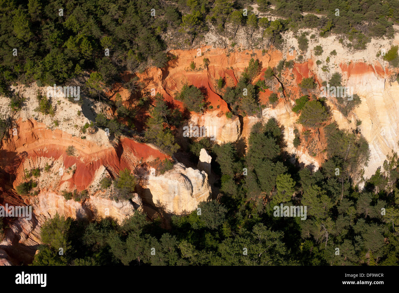 VISTA AEREA. Scogliera con strati di ocra multicolore in netto contrasto con il baldacchino circostante. Rustrel, Lubéron, Vaucluse, Provenza, Francia. Foto Stock