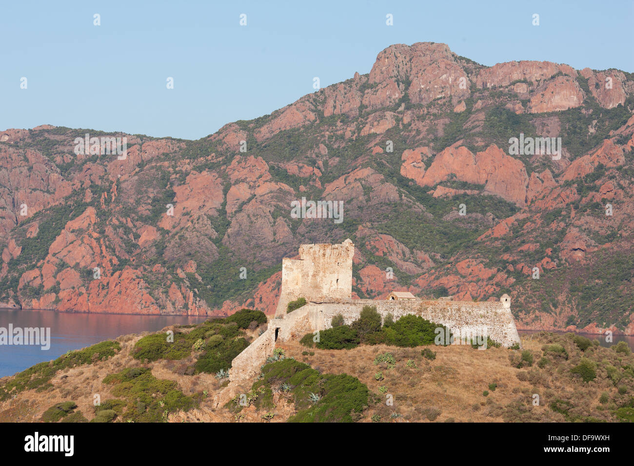 La torre genovese si affaccia sul Golfo di Girolata, con sullo sfondo la massiccia scogliera di roccia vulcanica rossa di Scandola. Osani, Corsica, Francia. Foto Stock