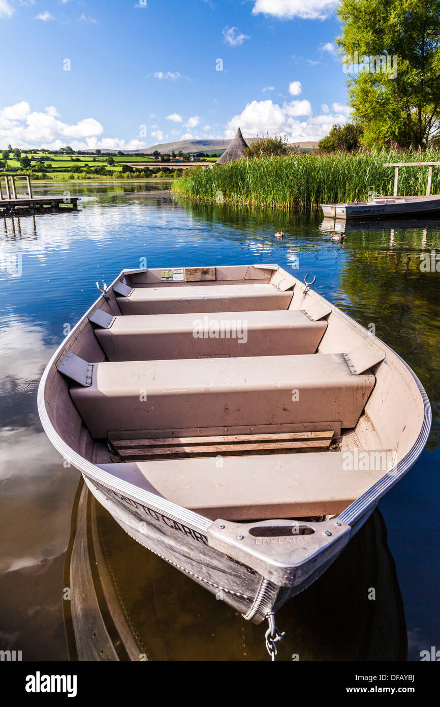 Barca a remi ormeggiate a Llangors Lake nel Parco Nazionale di Brecon Beacons, Galles con il crannog nella distanza. Foto Stock