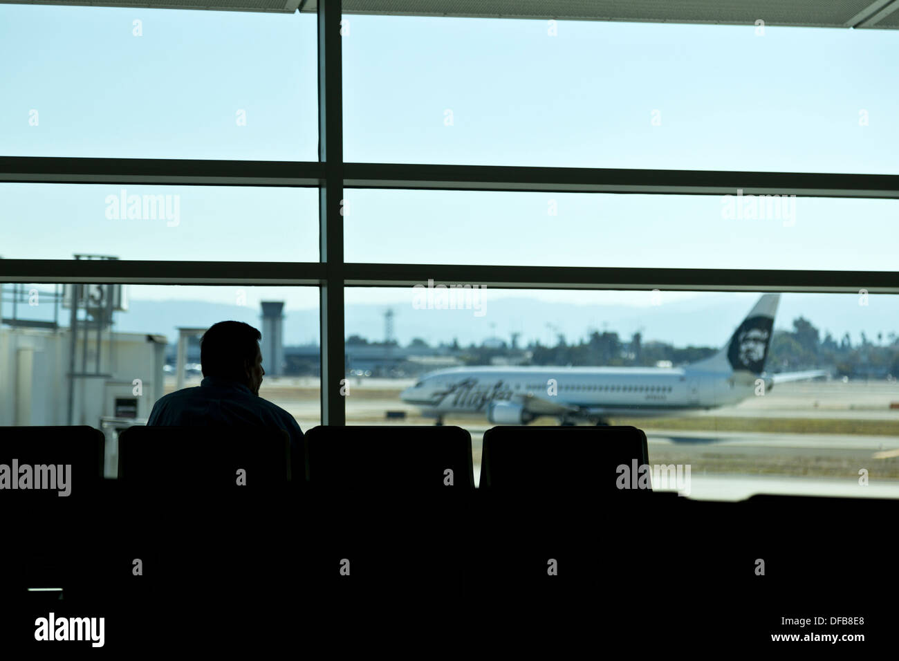 Uomo in attesa nella sala partenze al Terminal di un aeroporto internazionale di San Jose come un aereo taxi sulla pista, CALIFORNIA, STATI UNITI D'AMERICA Foto Stock