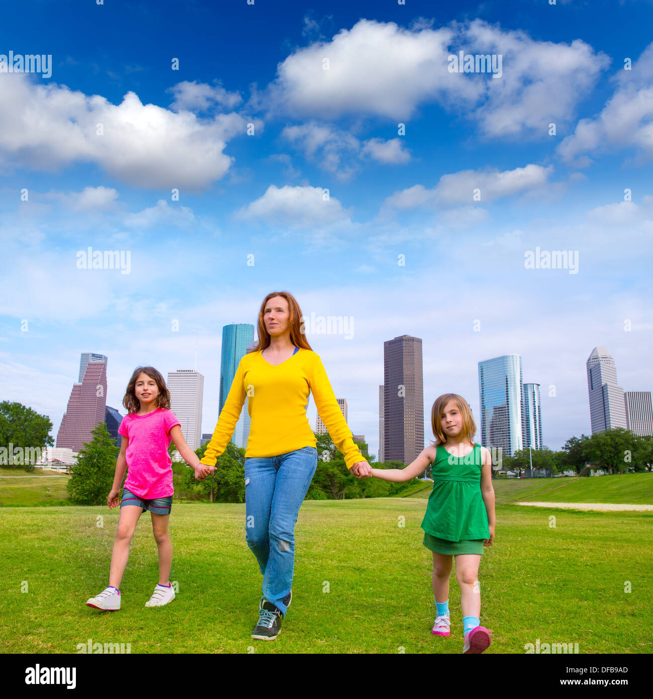 La madre e le figlie a piedi tenendo le mani sul moderno skyline della città oltre il parco Prato verde Foto Stock