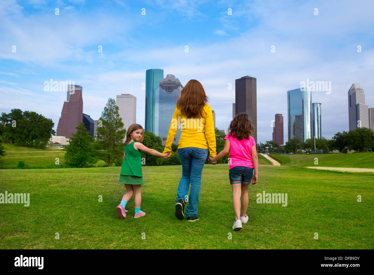 La madre e le figlie a piedi tenendo le mani sul moderno skyline della città oltre il parco Prato verde Foto Stock