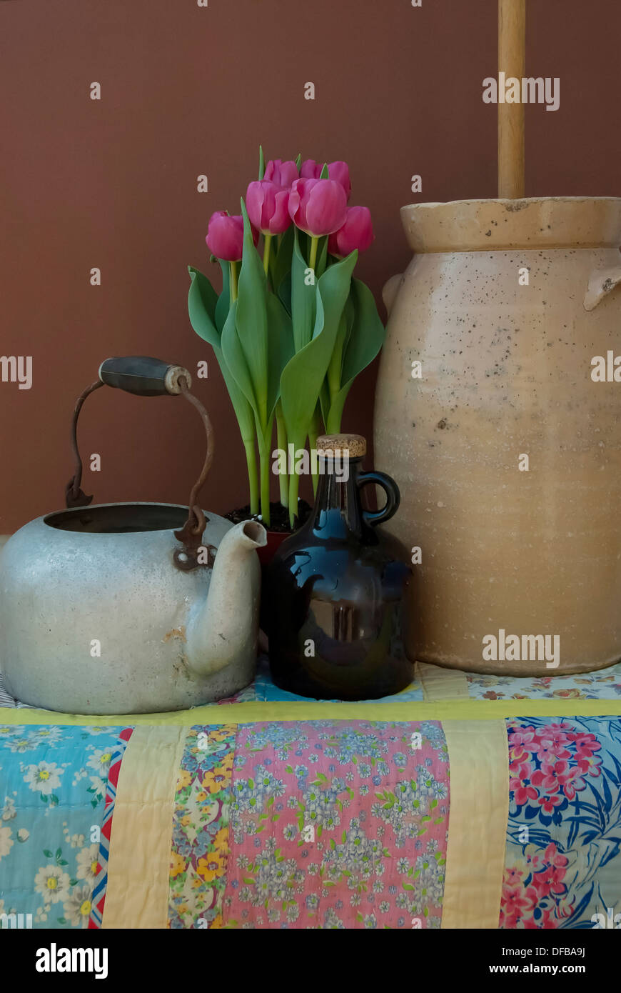 Un vecchio tè pentola brocca, zangola, rosa tulipani in un colorato fatto a mano trapunta. Foto Stock