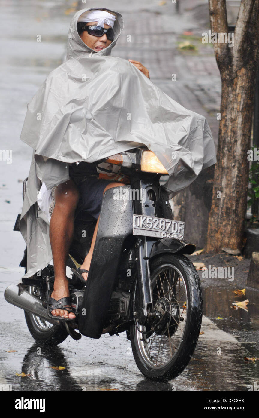 Legian Bali (Indonesia): un uomo alla guida di uno scooter sotto la pioggia,  proteggendo il suo figlio al di sotto di un panno di massa Foto stock -  Alamy