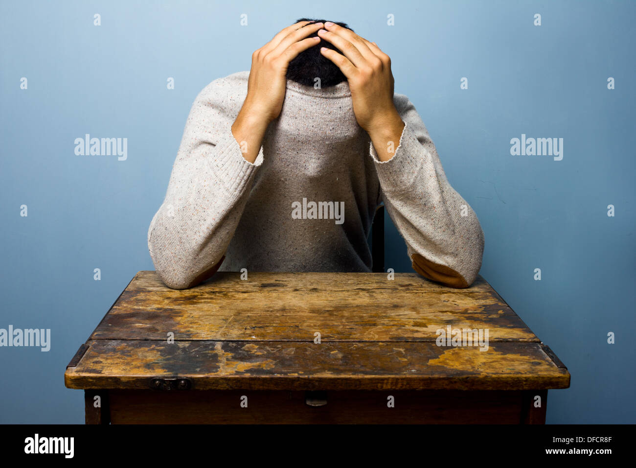 Giovane uomo alla scrivania si nasconde al suo interno il suo ponticello Foto Stock