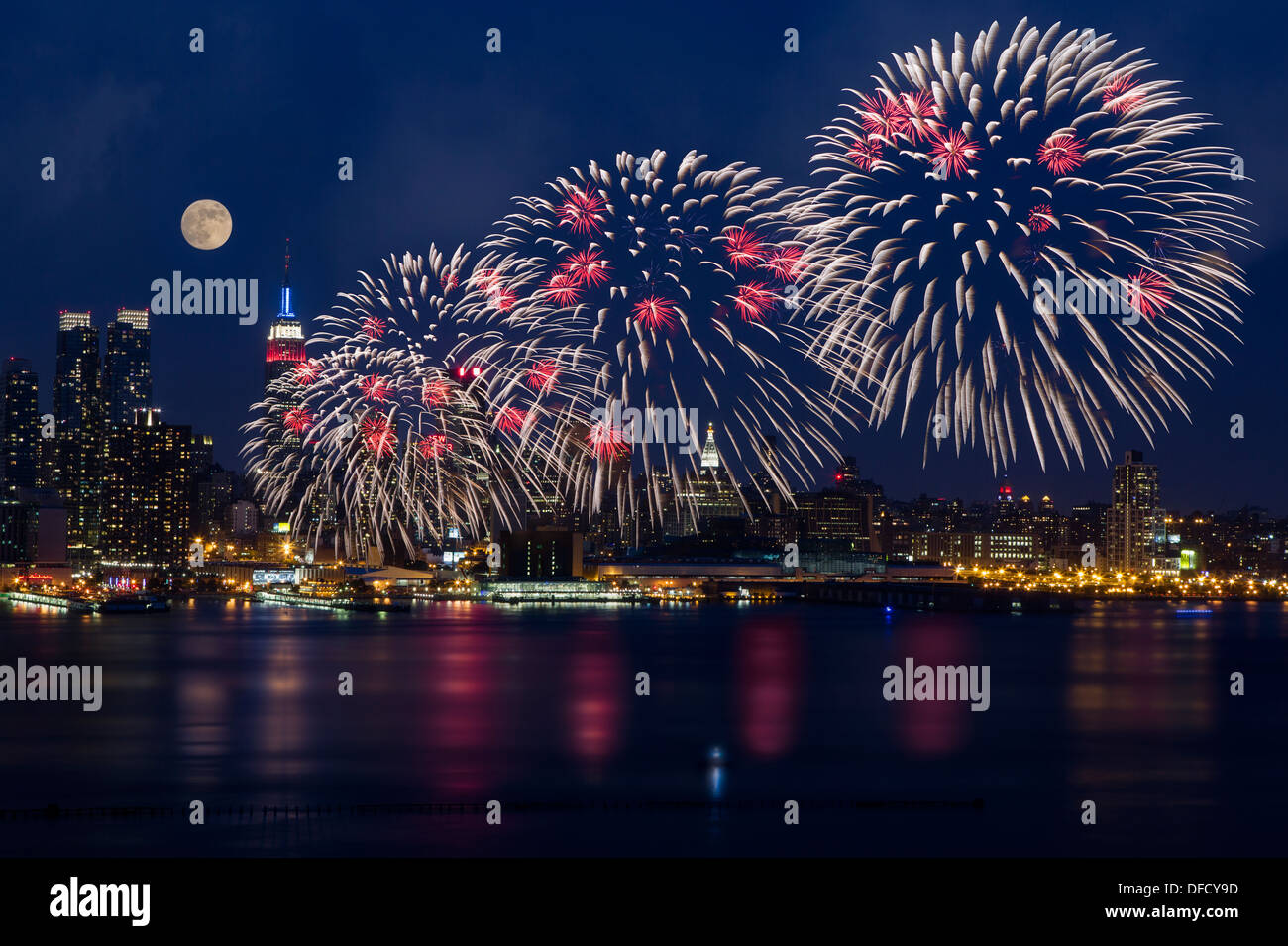 La luna piena che si innalzano per oltre sullo skyline di New York come il Macy's spettacolari fuochi d'artificio del 4 luglio festa spettacolo inizia. Foto Stock
