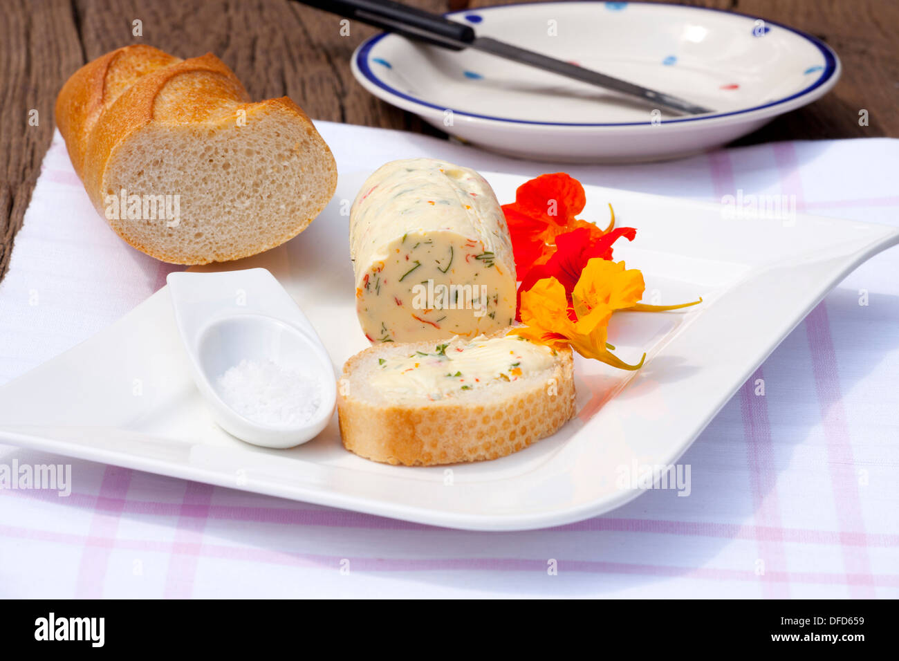 In casa nasturtium burro alle erbe su una piastra con un pezzo di baguette e sale di mare su una tavola in legno rustico Foto Stock