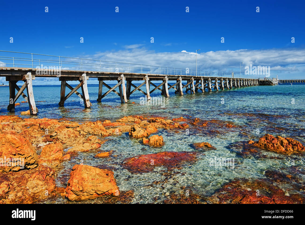 Paesaggio di mare con il molo di legno e pietre di colore arancione Foto Stock