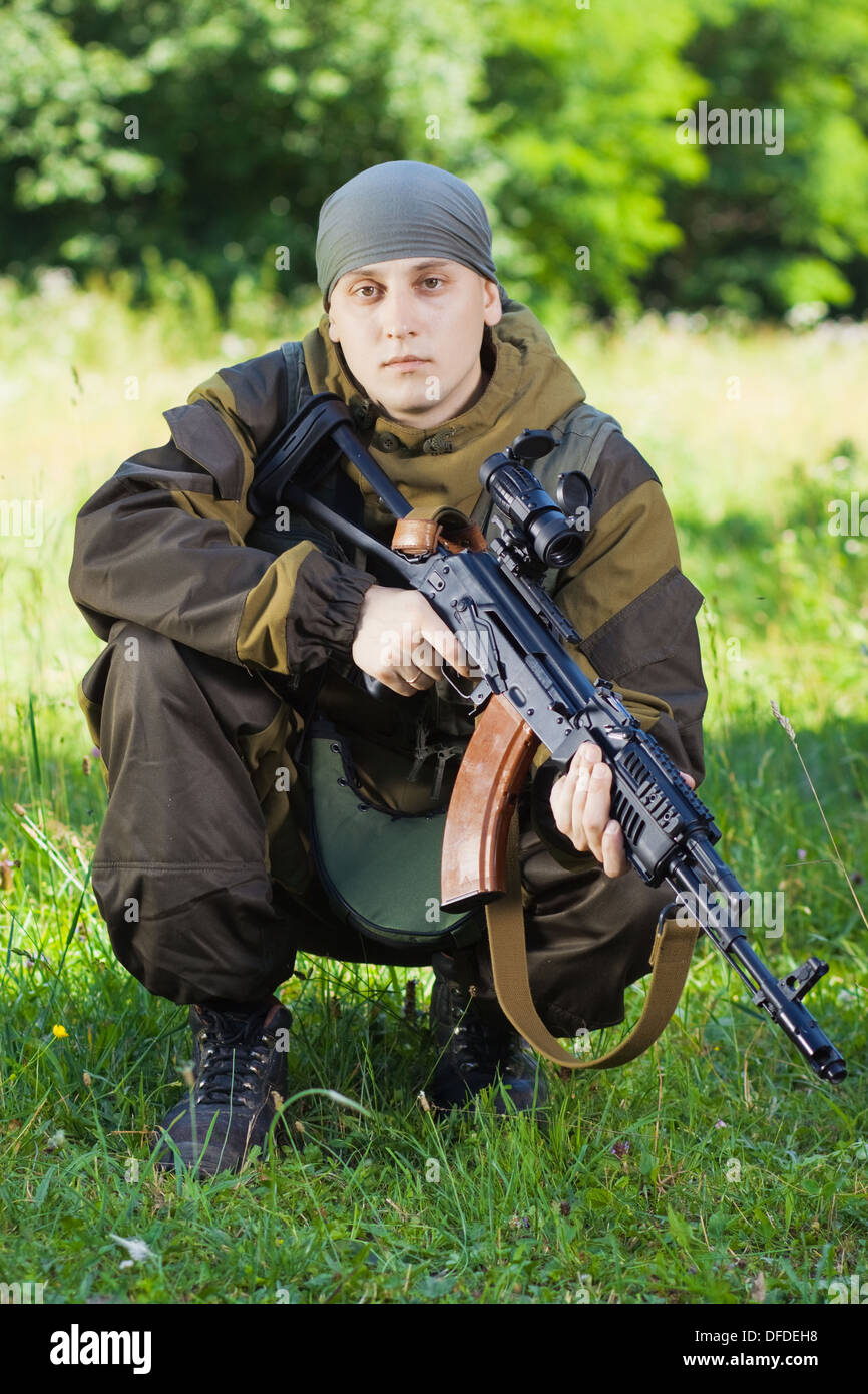 Soldato in camuffamento con un kalashnikov fucile da assalto seduto sull'erba Foto Stock