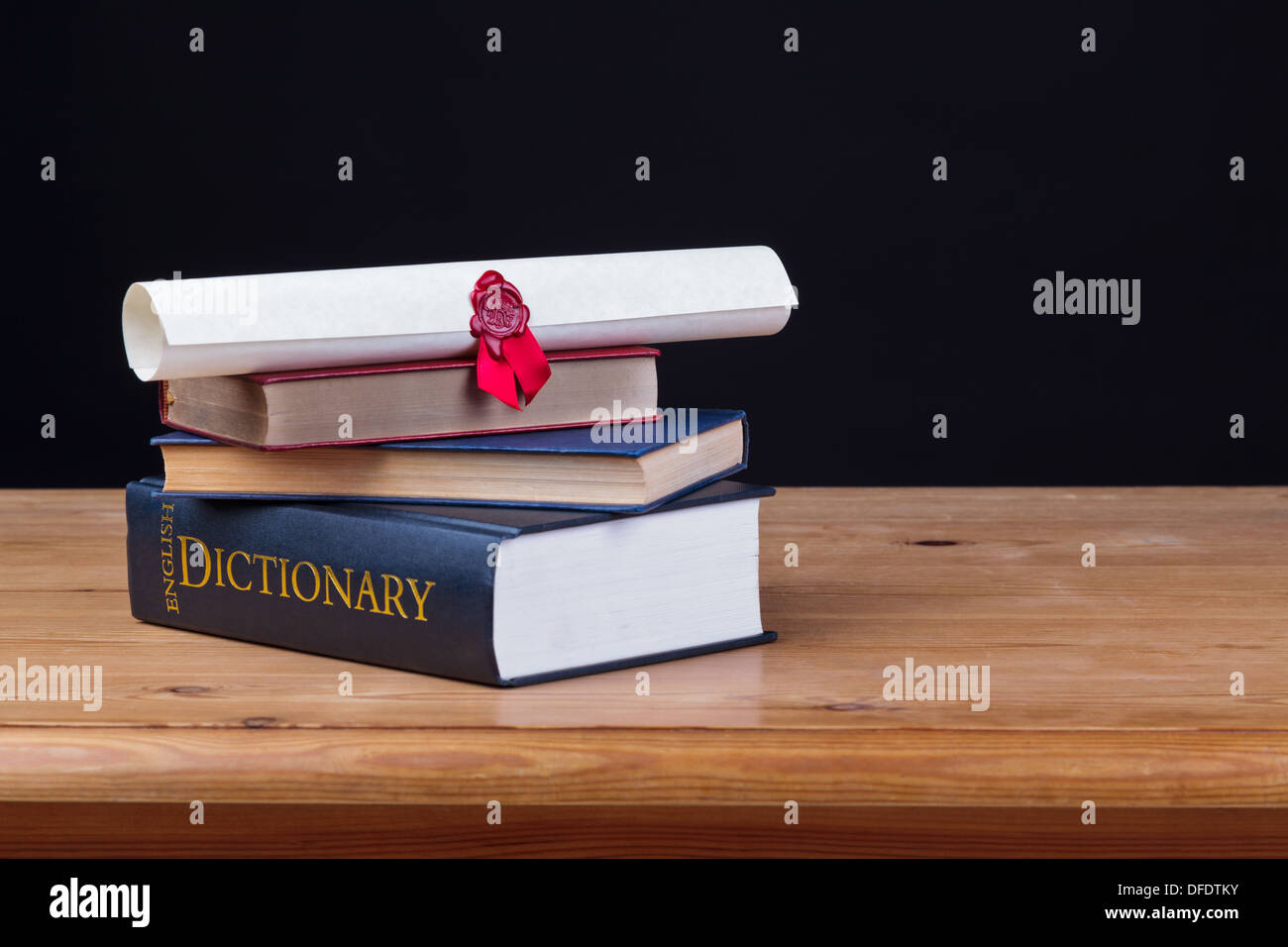 Banco di scuola con il dizionario e un diploma contro uno sfondo nero, aggiungi il proprio testo. Foto Stock