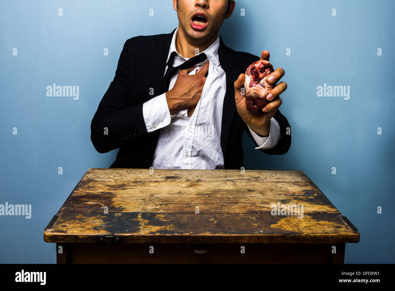 Giovane imprenditore sta tenendo il suo petto dolore mentre tiene un animale crudo il cuore nella sua altra mano a simboleggiare un attacco di cuore Foto Stock