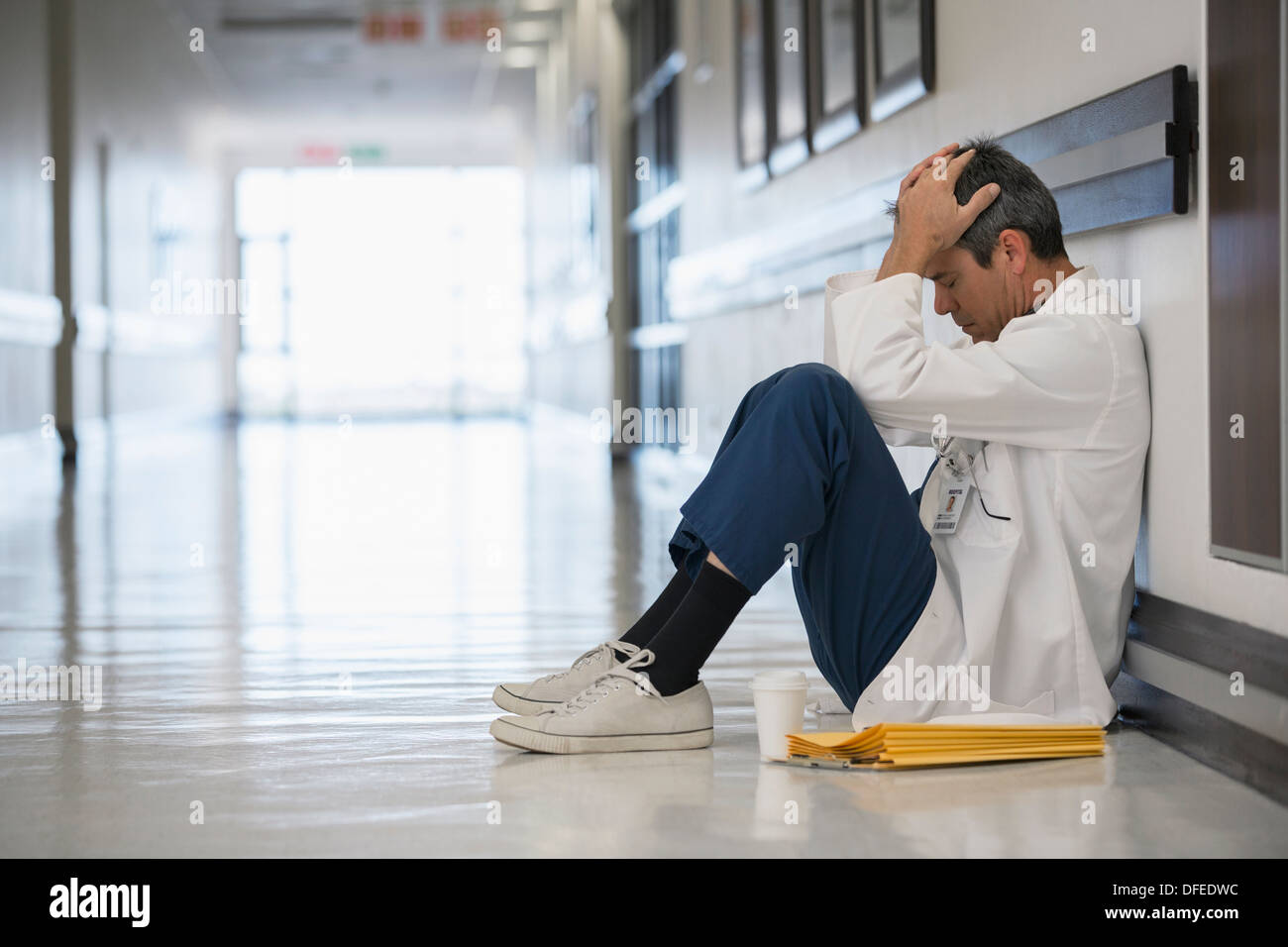 Medico seduto sul pavimento nel corridoio di ospedale con testa in mani Foto Stock