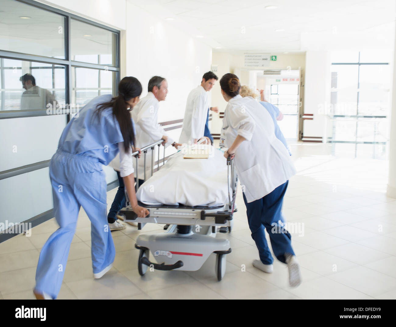 I medici rushing paziente sulla barella verso il basso corridoio ospedale Foto Stock