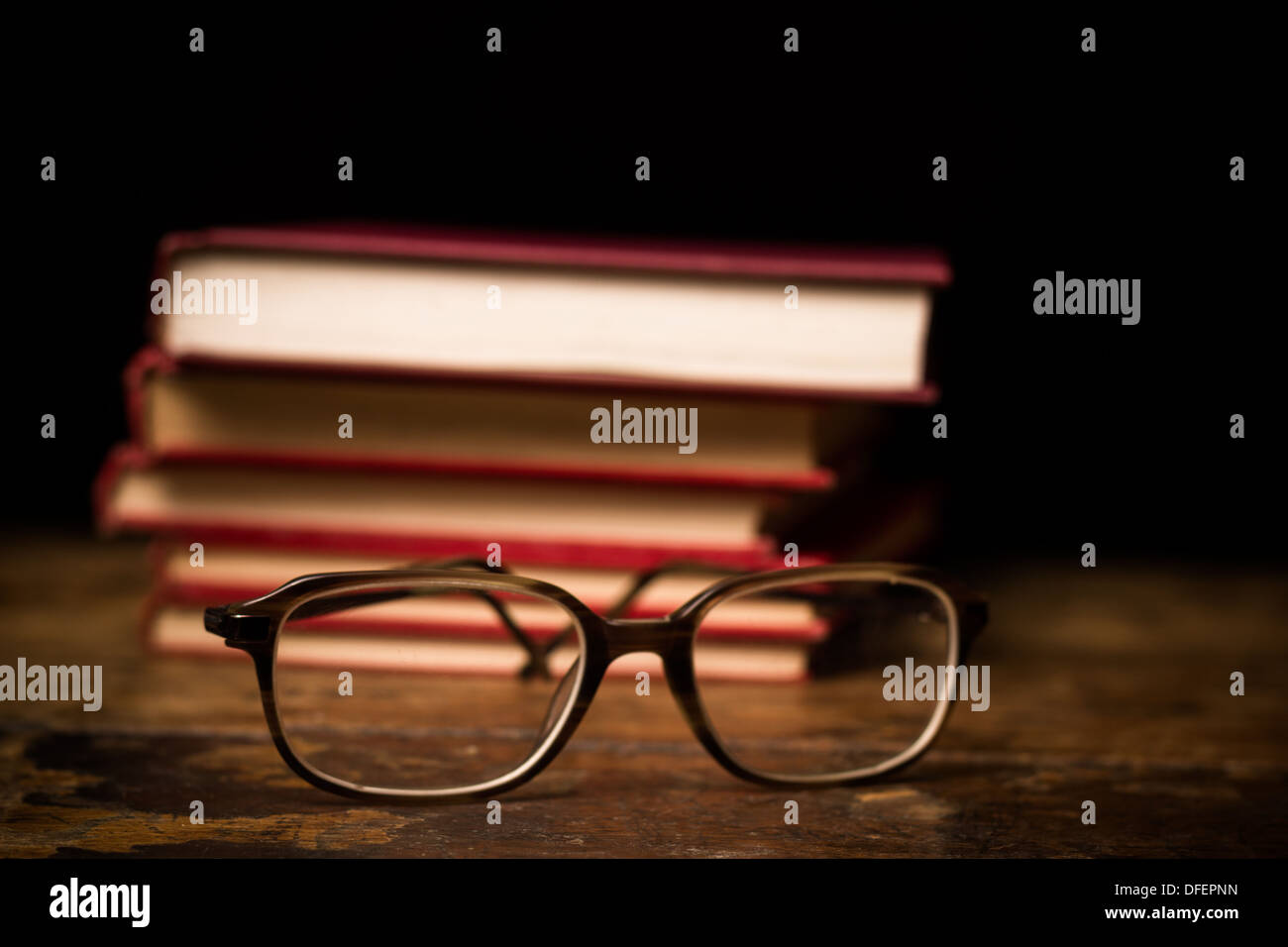 Paio di Occhiali sulla superficie di legno con la pila di libri in background Foto Stock