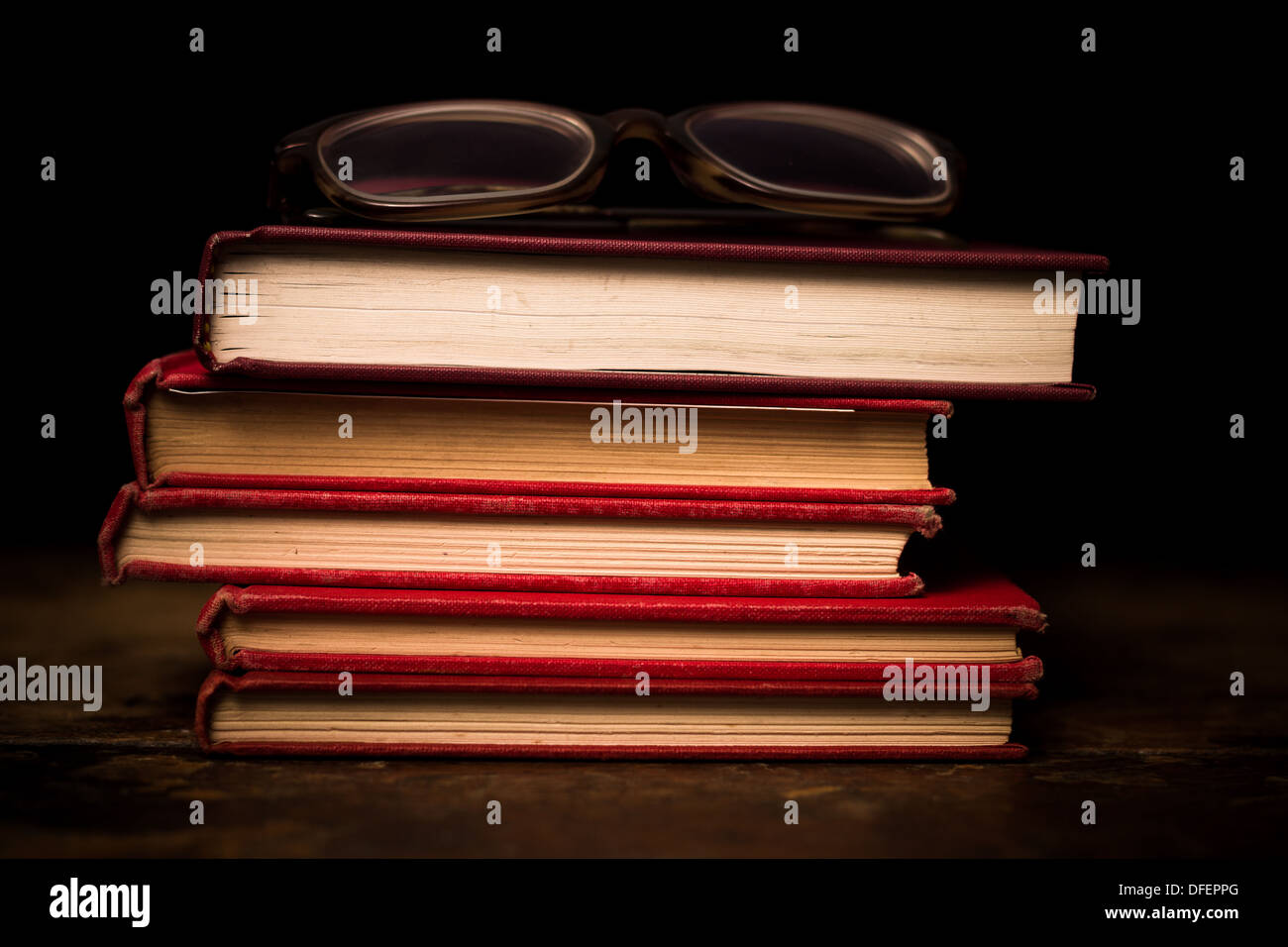 Pila di libri rossi sulla superficie di legno con un paio di occhiali Foto Stock