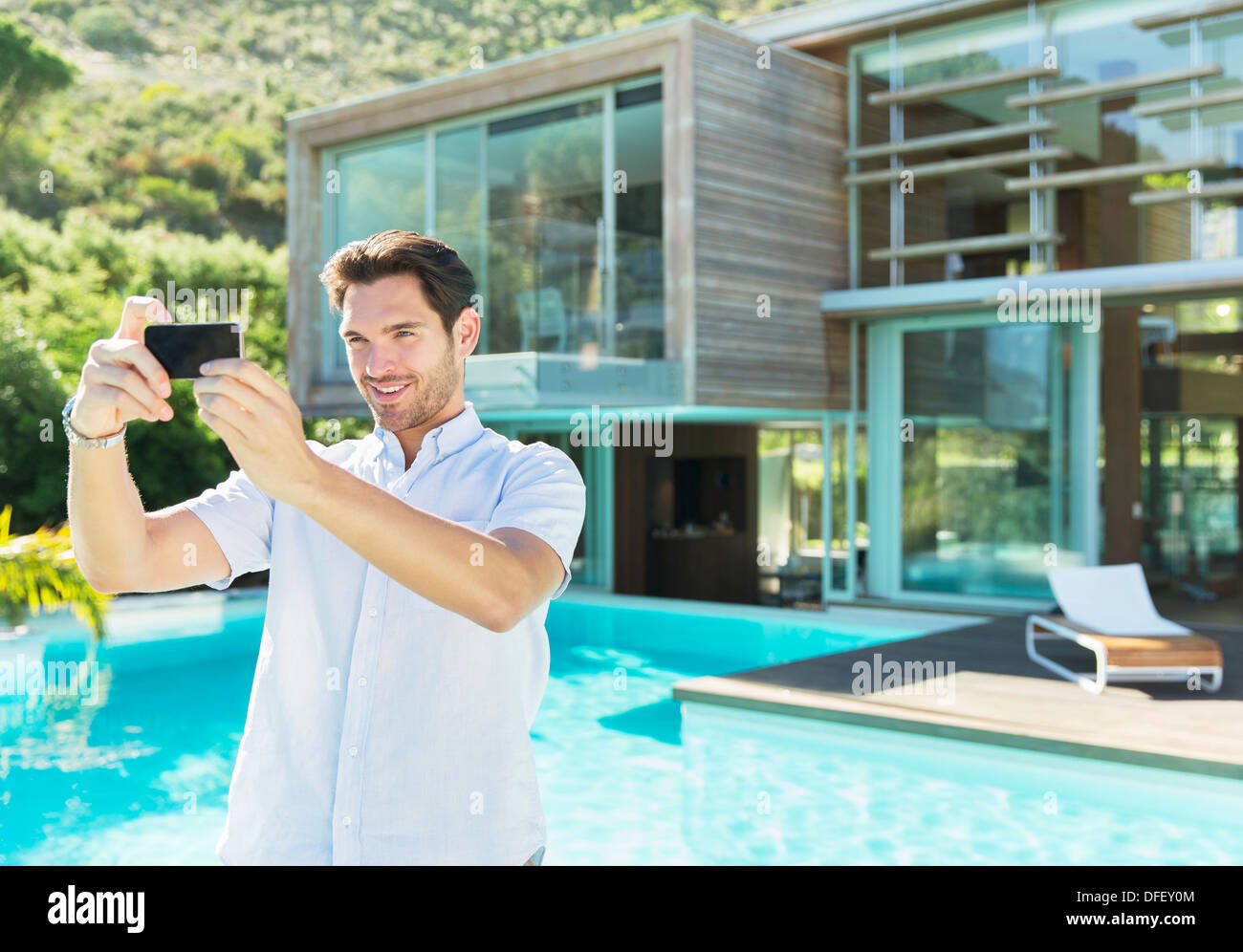 L'uomo prendendo autoritratto con la fotocamera del telefono a bordo piscina Foto Stock