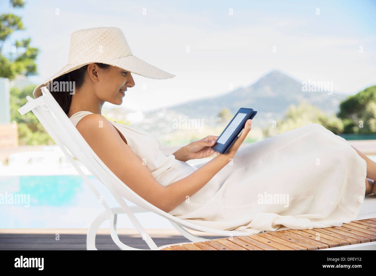 Donna con tavoletta digitale sulla sedia a sdraio a bordo piscina Foto Stock