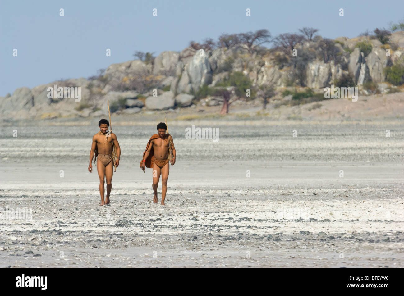 San bushman trackers attraversando a piedi il incrinato pan lontano dalle antiche affioramento di granito di Kubu Island (Lekhubu), Makgadikgadi Pan, Botswana Foto Stock